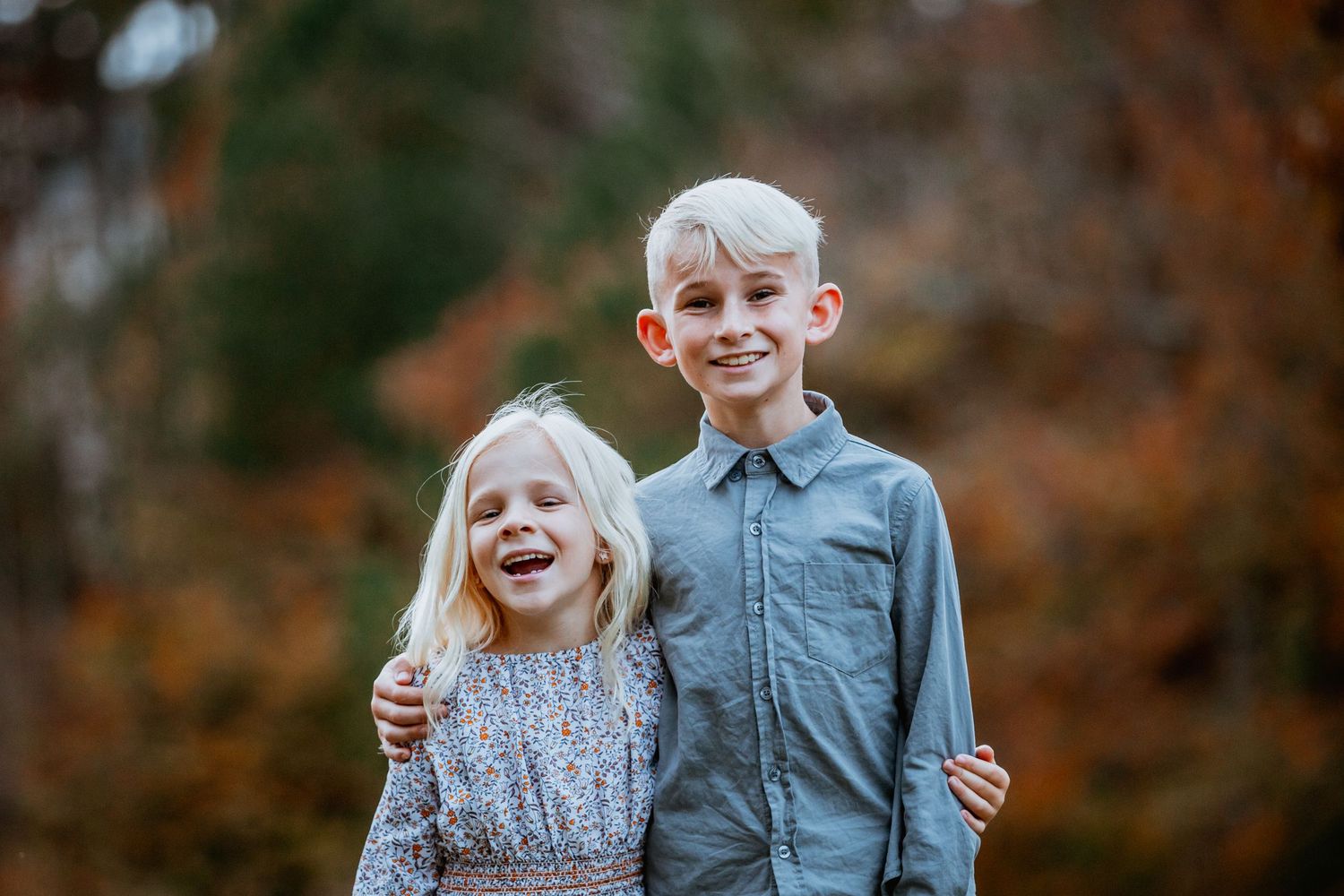 Smiling blonde siblings hugging outdoors during autumn family portrait session.