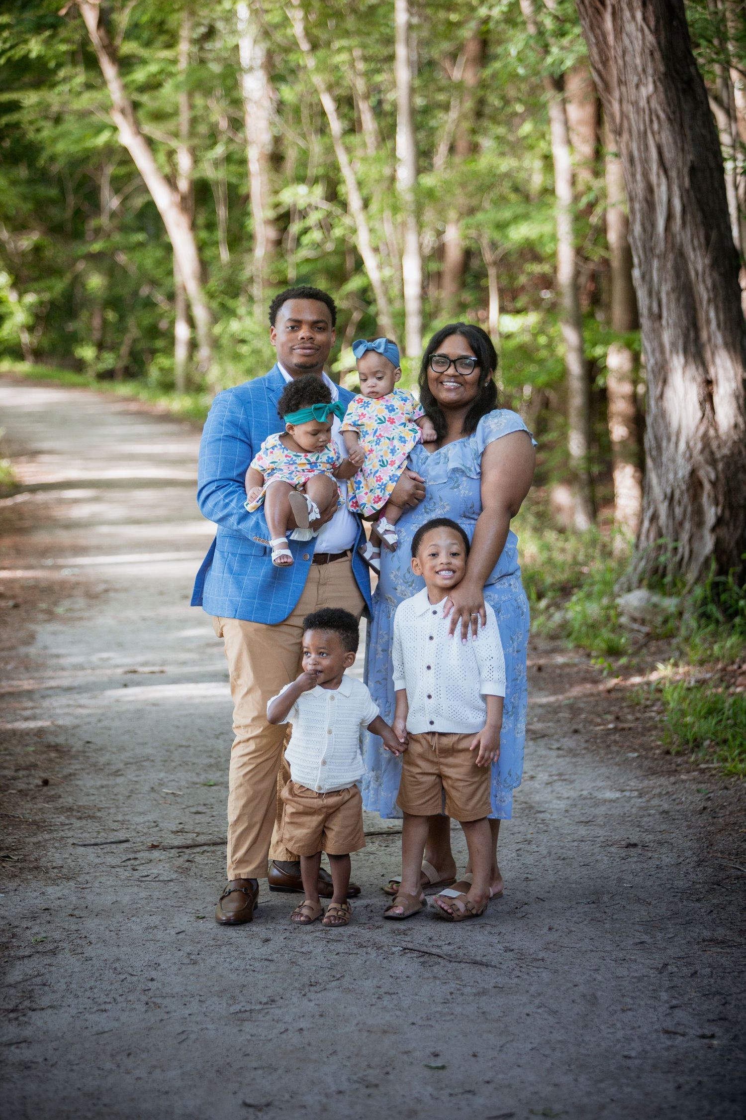 Happy family of five posing on a wooded path, parents in blue outfits with three young children.