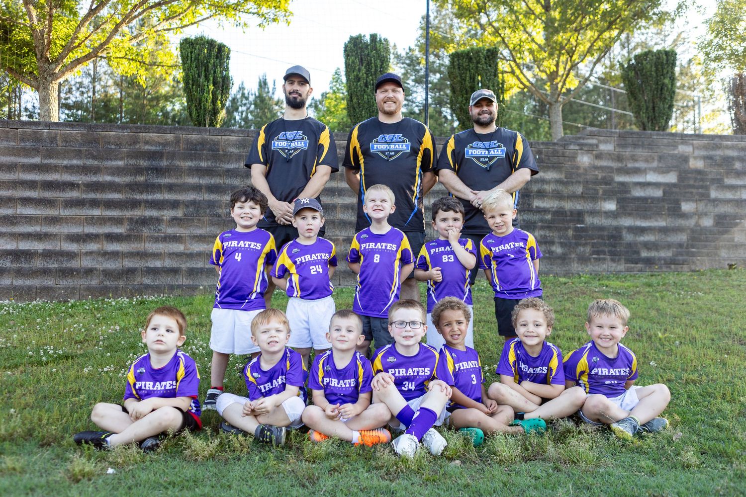 Youth flag football team in purple jerseys poses with three coaches for group team photo outside.