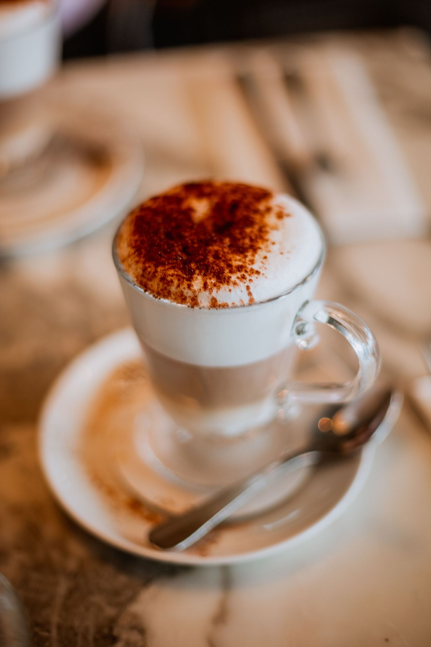 Layered latte macchiato in a glass cup topped with cocoa powder on a marble cafe table.