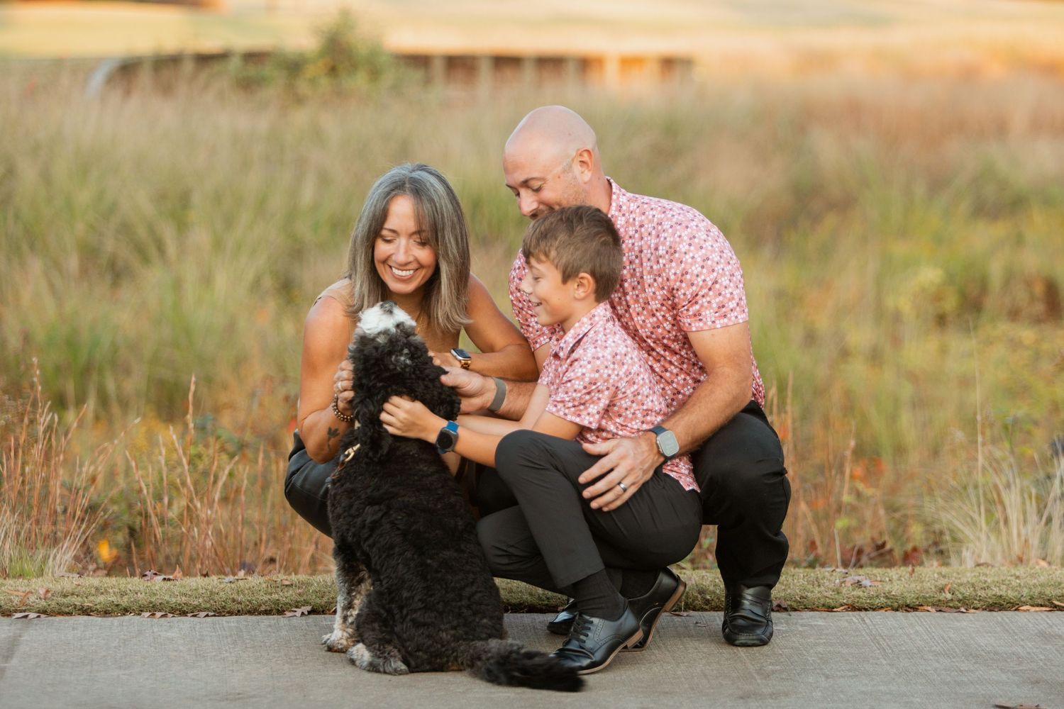 Family crouches down to pet their black and white dog during autumn outdoor photo session.