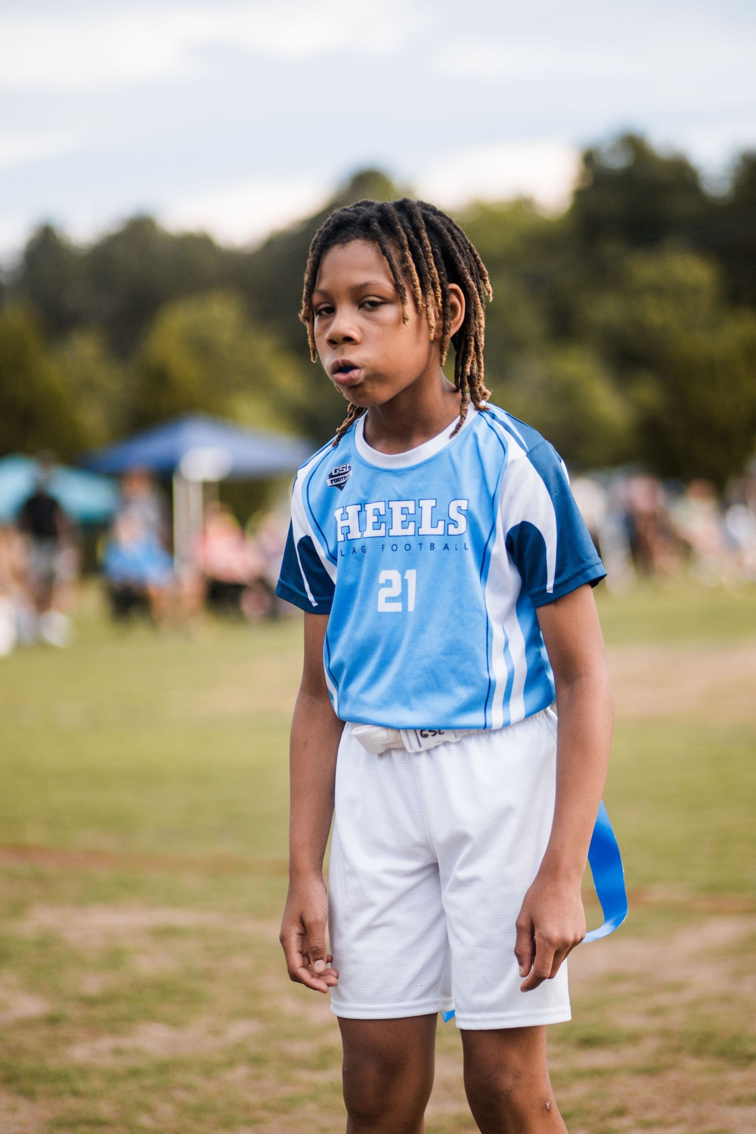 Young boy in Heels #21 blue flag football uniform standing on grass field.