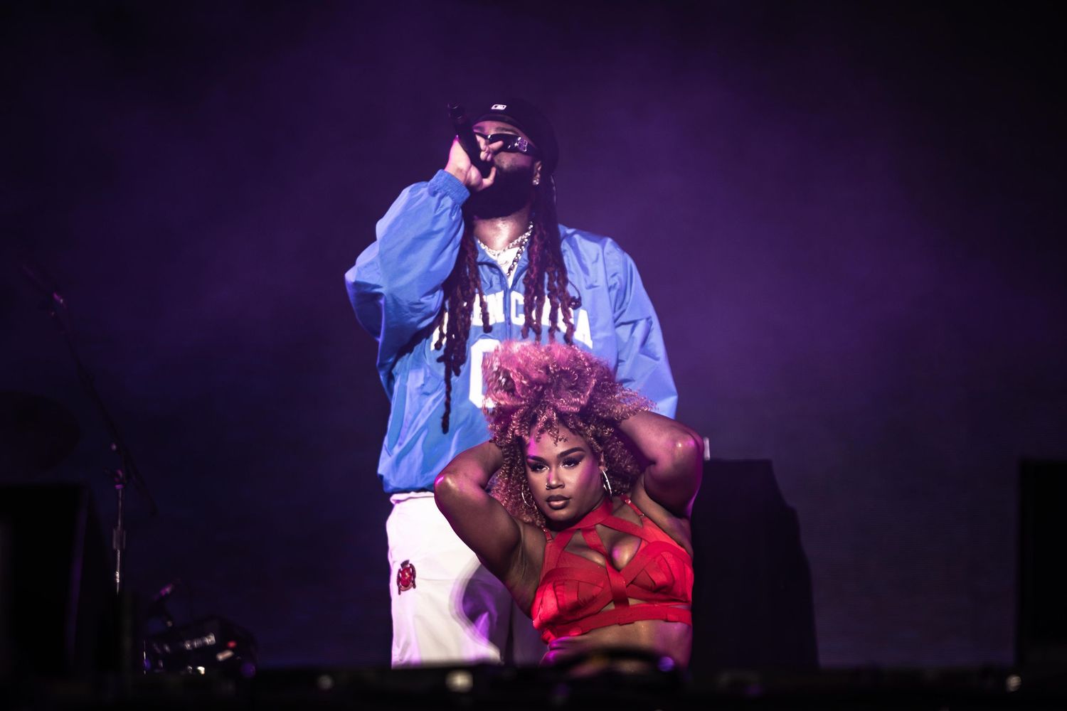 Male rapper performing on stage with female dancer seated below.