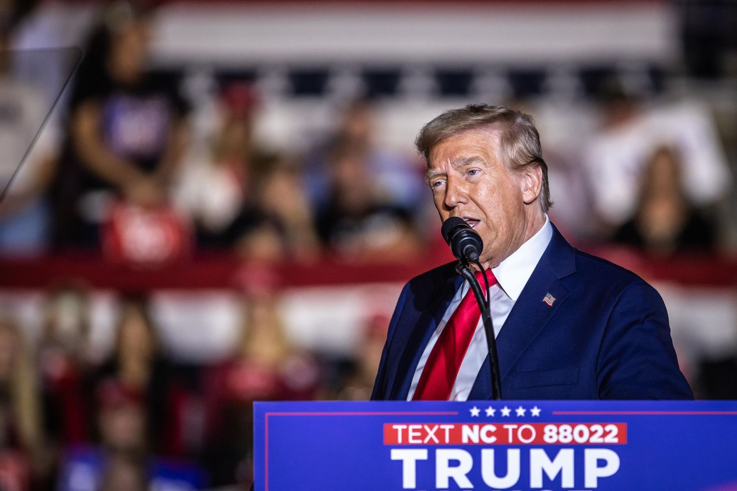 Donald Trump speaks at a campaign rally in North Carolina at a podium with a Trump Vance 2024 sign.