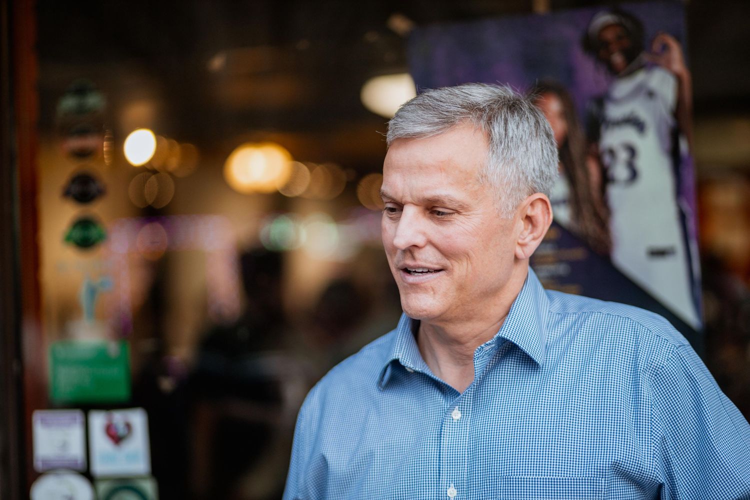 Older man with gray hair smiling outdoors near a sports memorabilia store.
