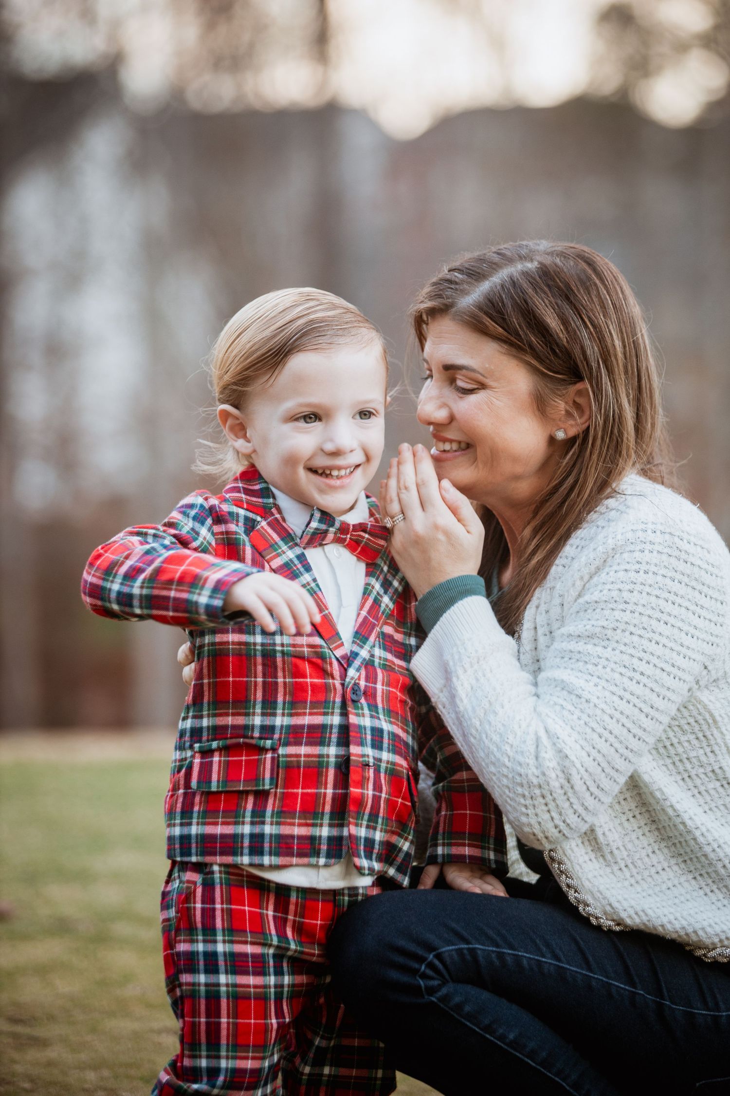 Mother and young son in red plaid suit sharing a joyful moment outdoors.