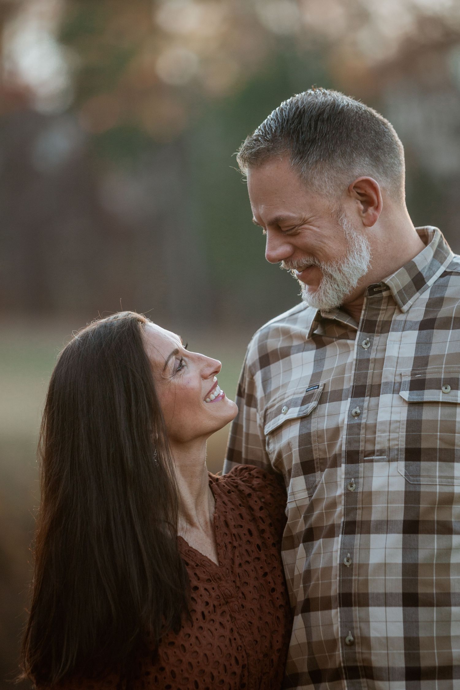 Happy couple sharing a romantic moment outdoors, woman in brown dress and man in plaid shirt.
