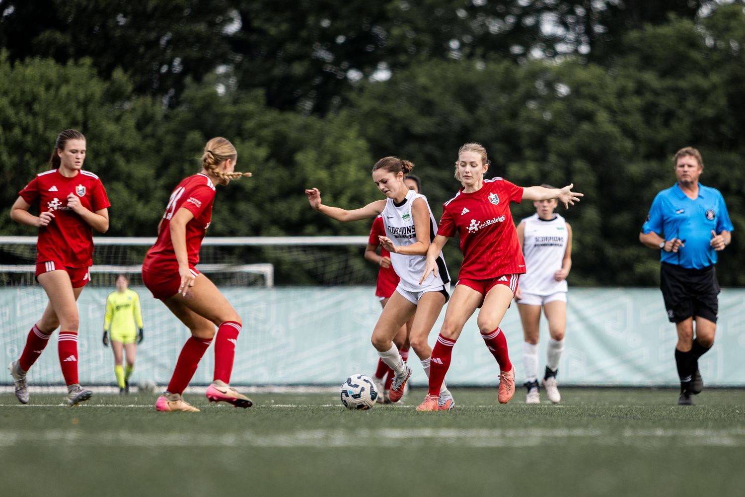 Female soccer players in red and white uniforms battle for possession during a competitive match.