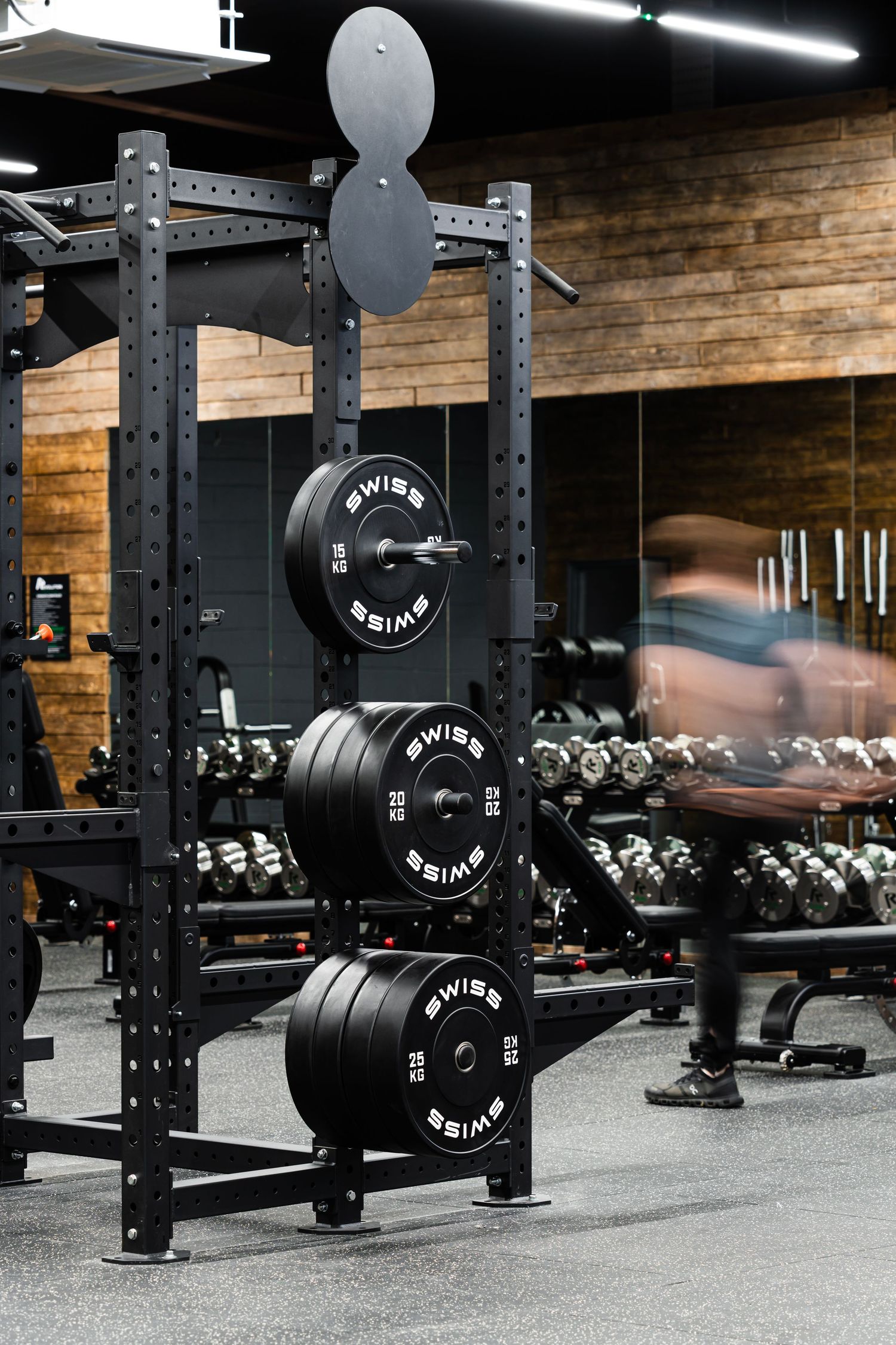 Weight plates stacked on squat rack with person movement in background