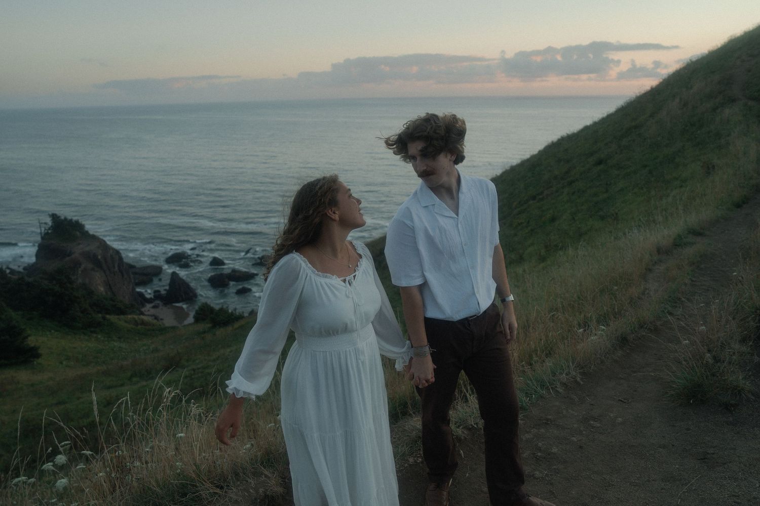 Couple walking hand in hand along God's Thumb trail during an Oregon Coast adventure session at sunset.