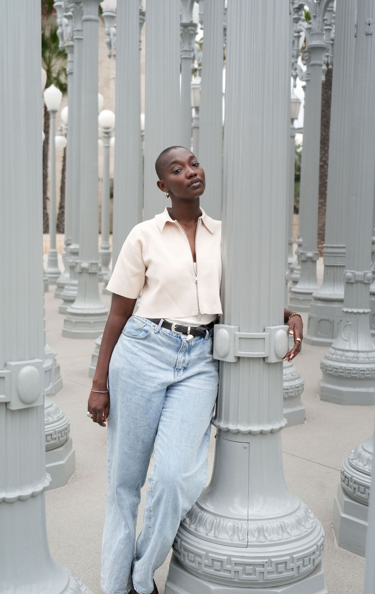 A woman in light jeans and beige shirt poses among gray lamp posts at LACMA's Urban Light installation.
