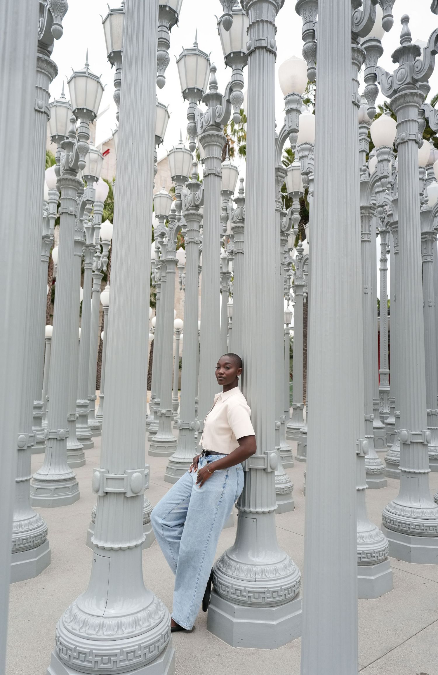 A woman in jeans and a white top leans against a lamp post at LACMA's Urban Light installation in Los Angeles.