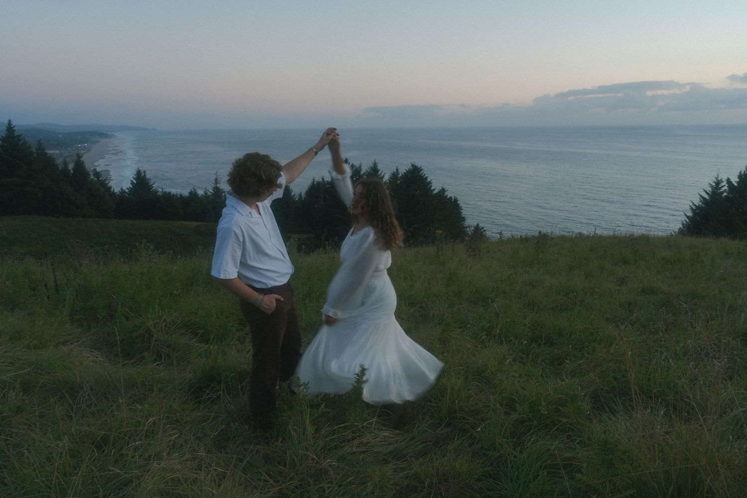Couple twirling together on a coastal cliff during a cinematic Oregon engagement session.