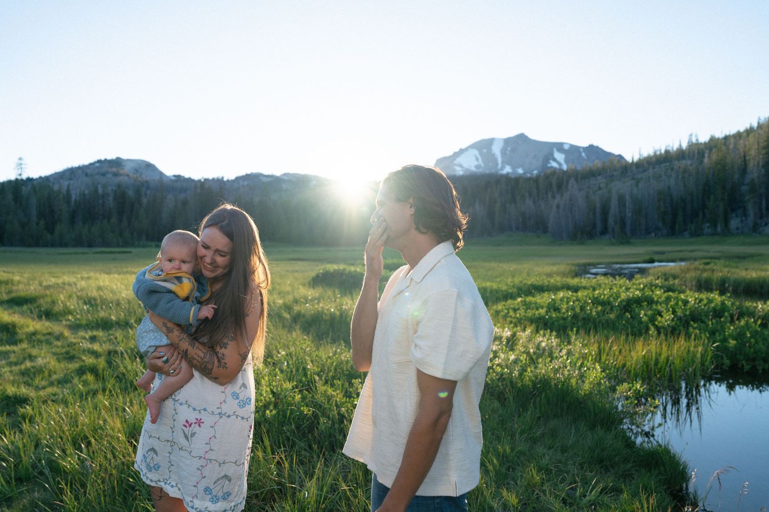 Family with baby enjoying a sunny mountain meadow with stream and peaks in background.