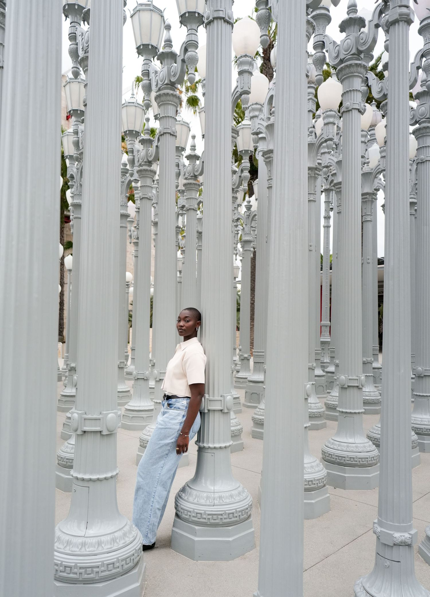 Person standing among gray vintage street lamps at LACMA Urban Light art installation in Los Angeles.