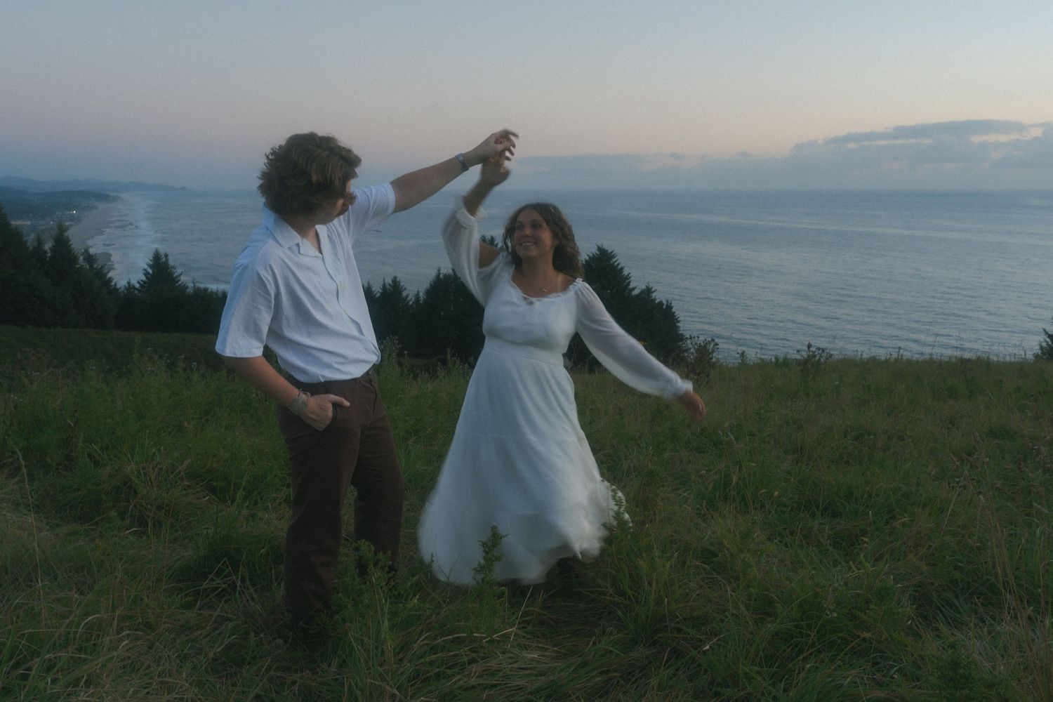 Couple twirling together on a coastal cliff during a cinematic Oregon engagement session.