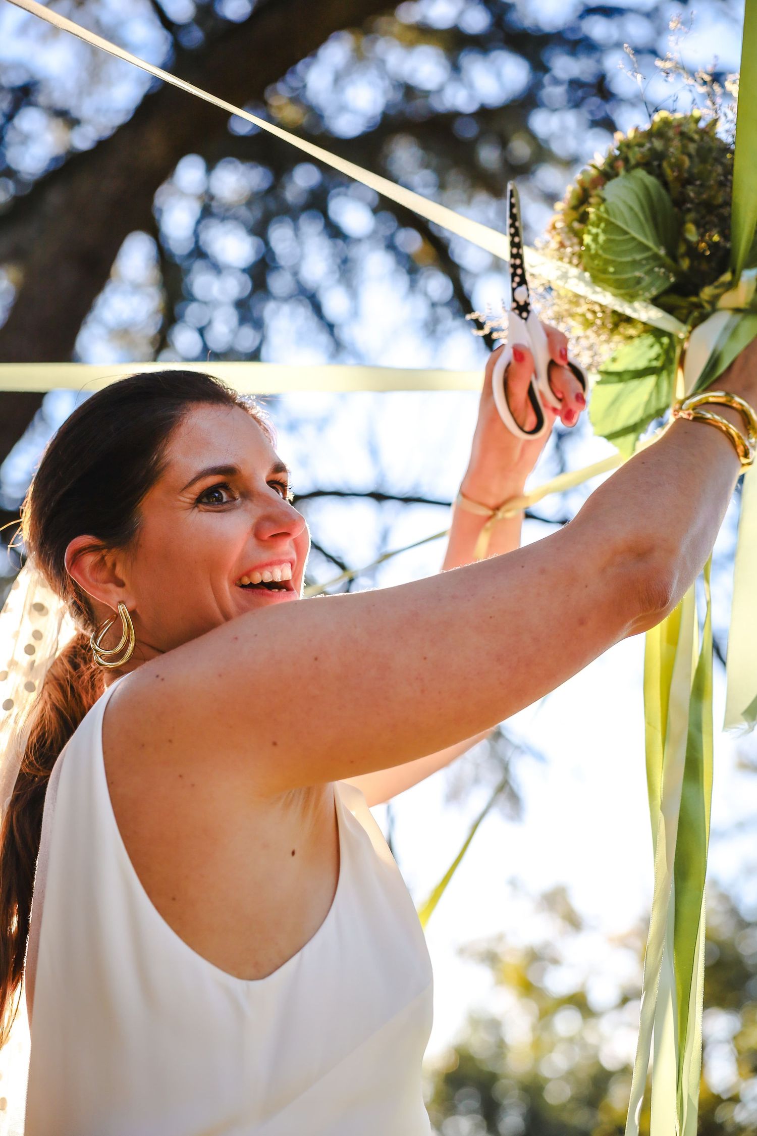Gros plan sur la mariée coupant un ruban du bouquet pour la future mariée. Tradition de mariage conviviale et élégante capturée sur le vif.