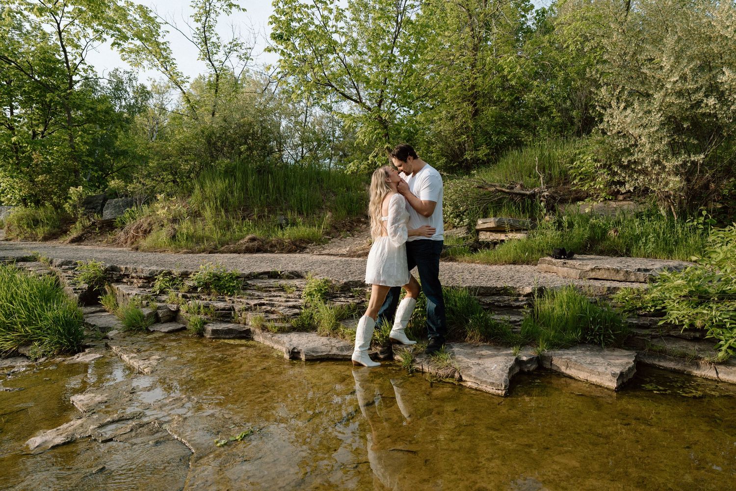 Couple sharing a romantic moment on stepping stones over a peaceful stream in a lush green garden.