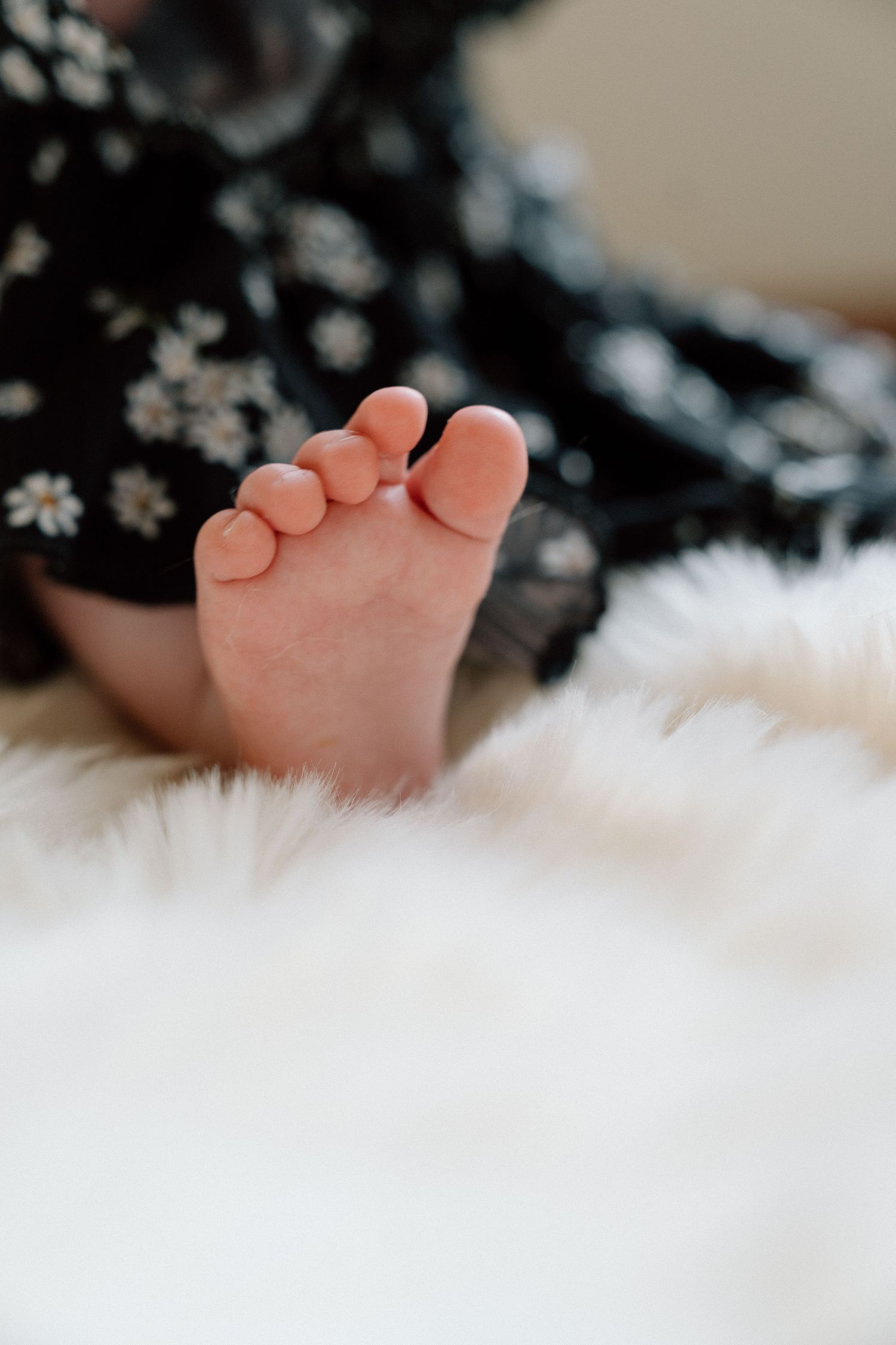 Close-up of a tiny baby foot resting on a soft white fluffy blanket, with a floral outfit visible in the background.
