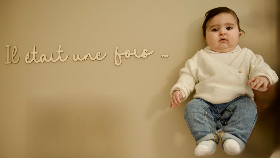 Portrait lifestyle d’un bébé en tenue beige, ambiance douce et chaleureuse en intérieur.