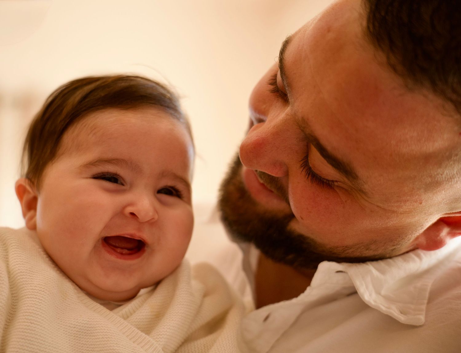Père tenant son bébé dans les bras, moment complice et naturel capturé en lumière douce.