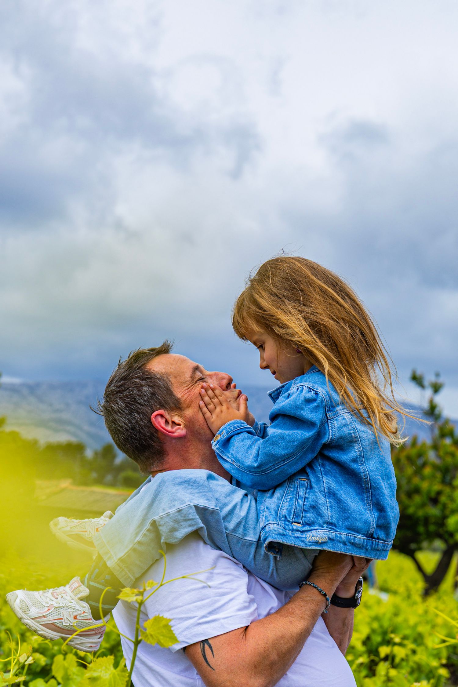 Père soulevant sa fille dans les vignes, instant complice et spontané en extérieur.