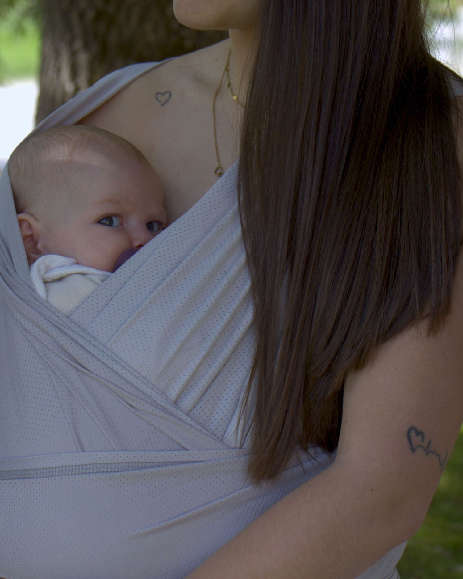 Bébé porté en écharpe contre sa mère, instant tendre et authentique capturé en extérieur.