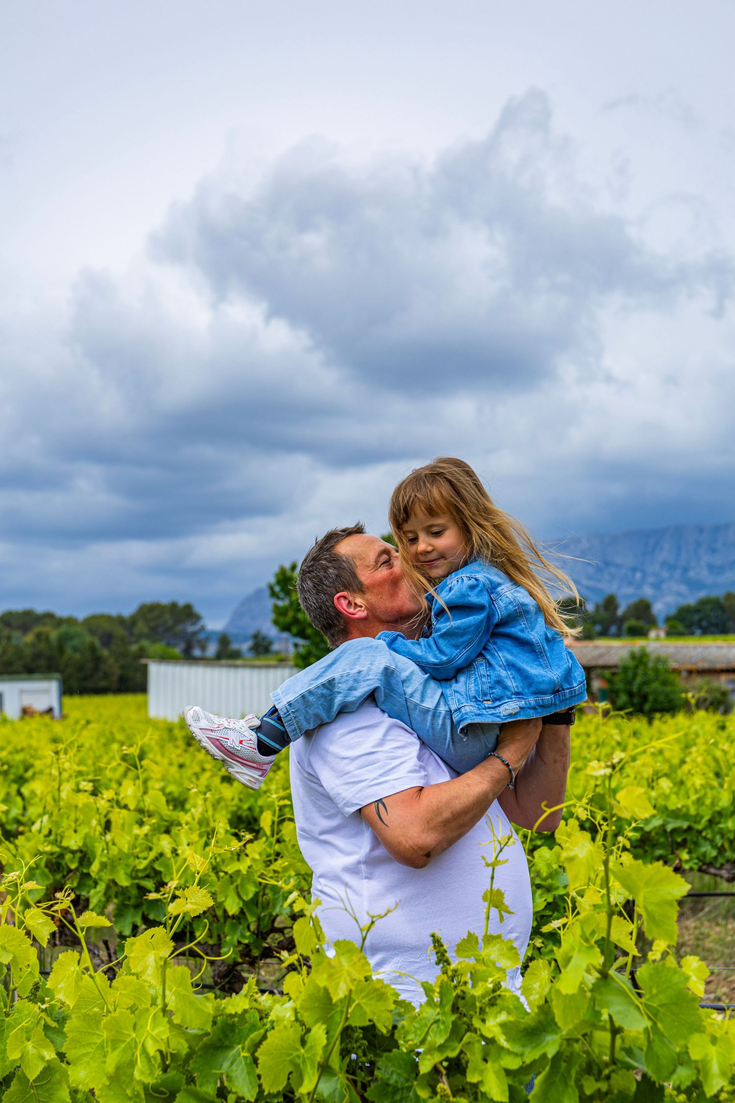 Père portant sa fille dans un champ fleuri, moment complice et authentique en famille.