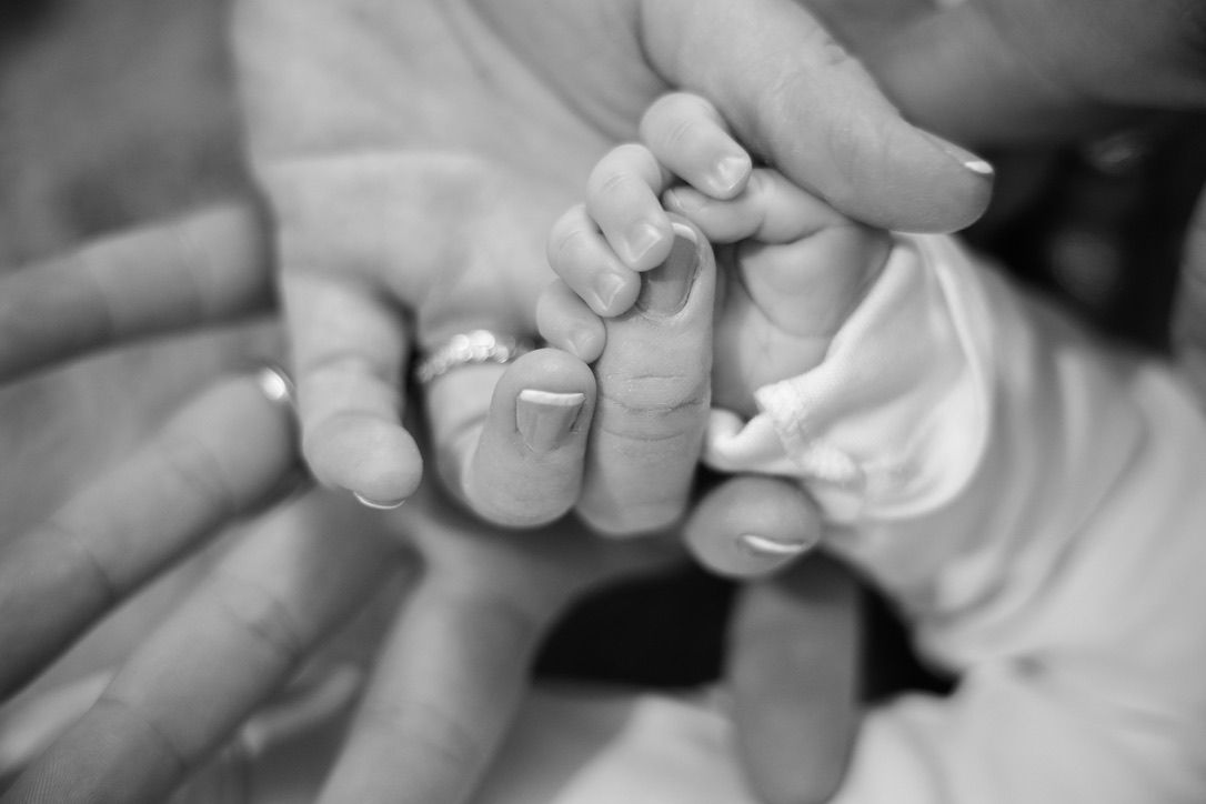 Mains d’un nouveau-né dans celles de ses parents, portrait famille noir et blanc intemporel.