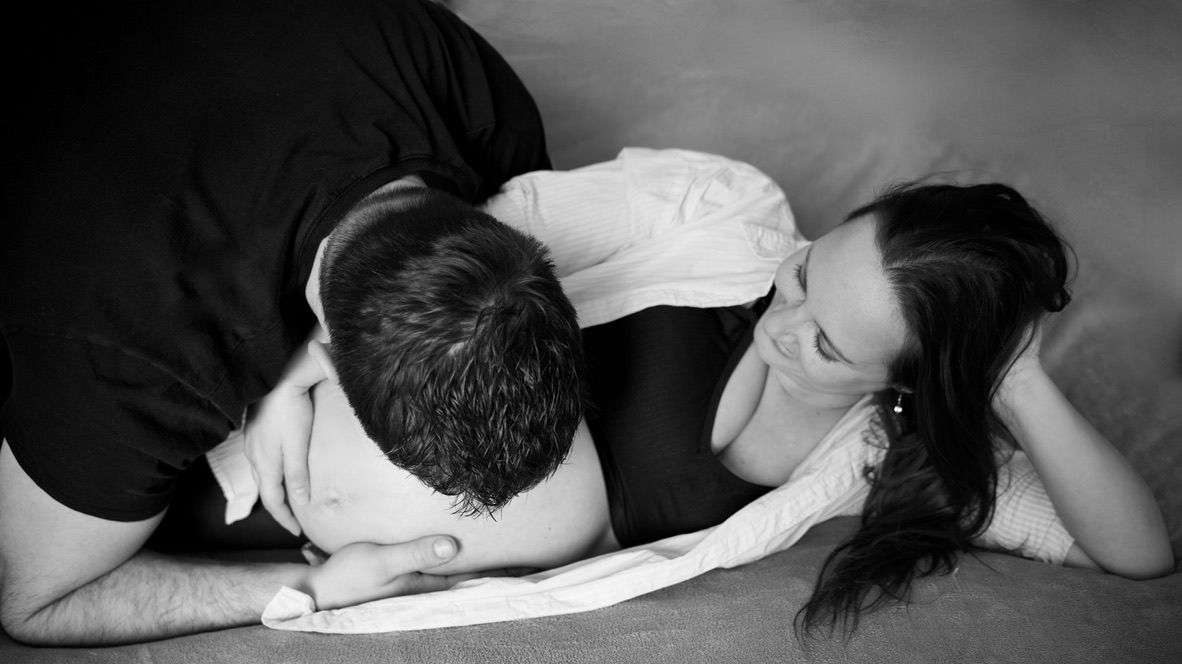 Futurs parents allongés ensemble en noir et blanc, portrait maternité artistique et complice.