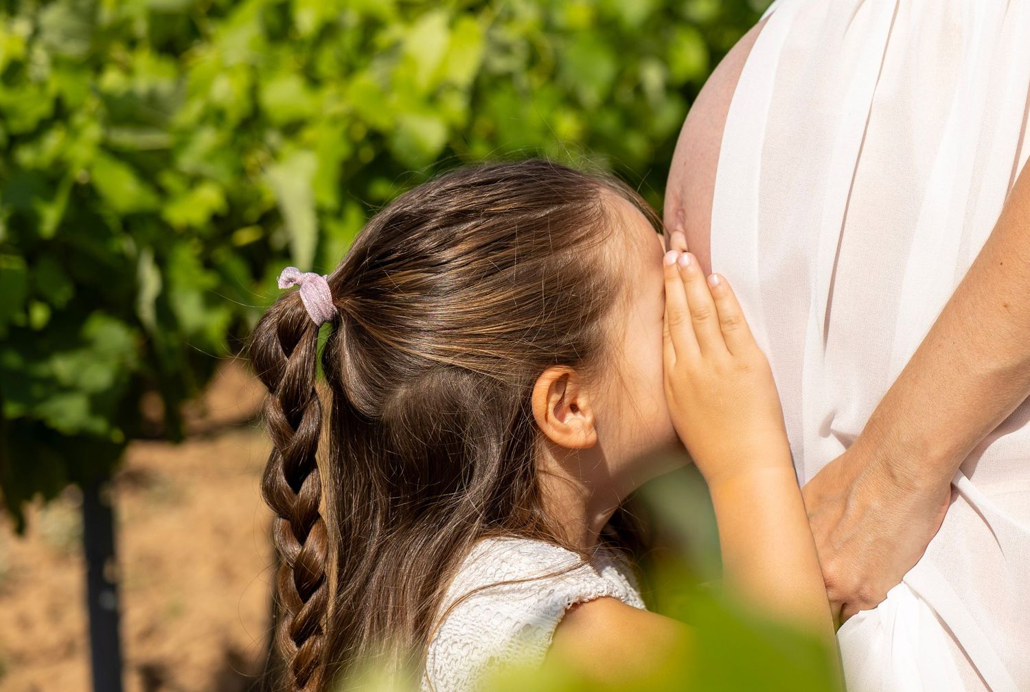 Enfant embrassant le ventre de sa maman pendant une séance photo grossesse dans les vignes