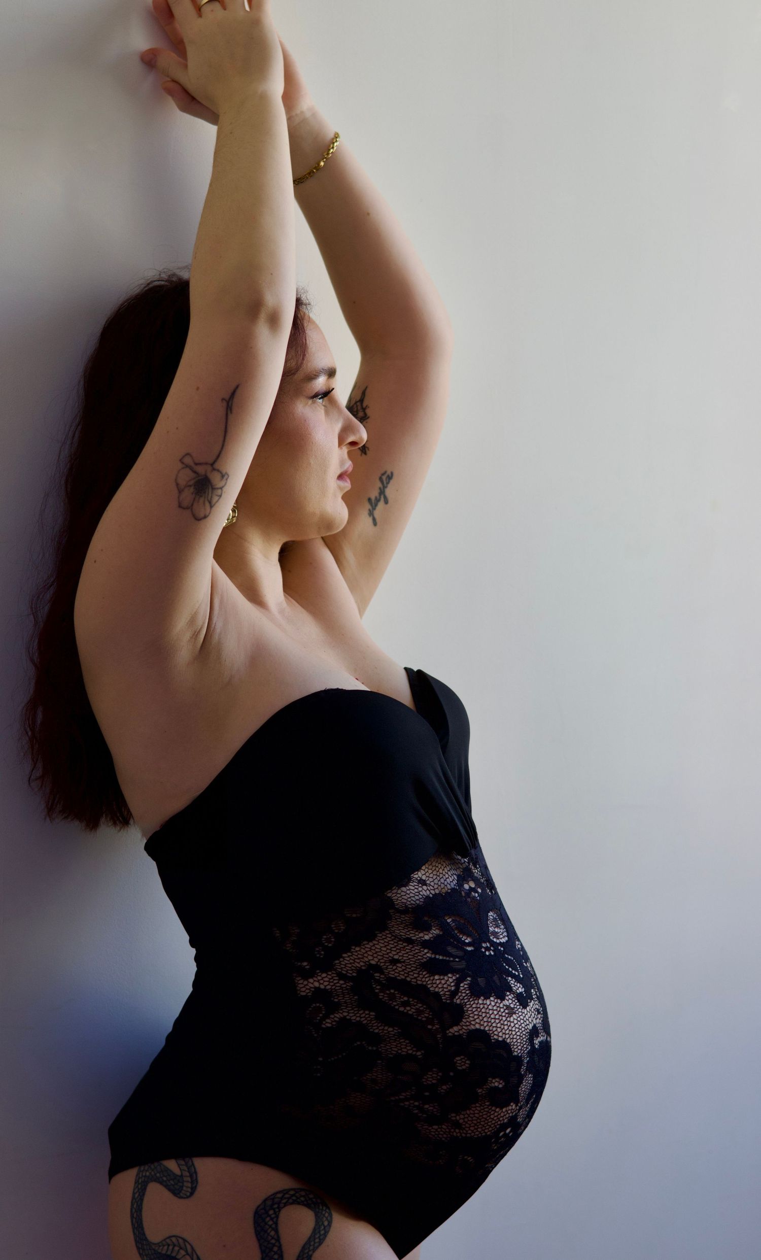Future maman levant les bras pendant une séance grossesse artistique en lumière naturelle.
