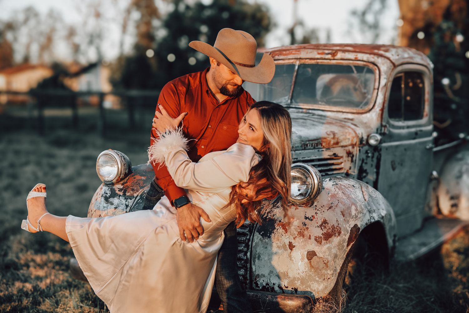 A couple embraces near a vintage truck during a romantic sunset photoshoot with warm autumn tones.