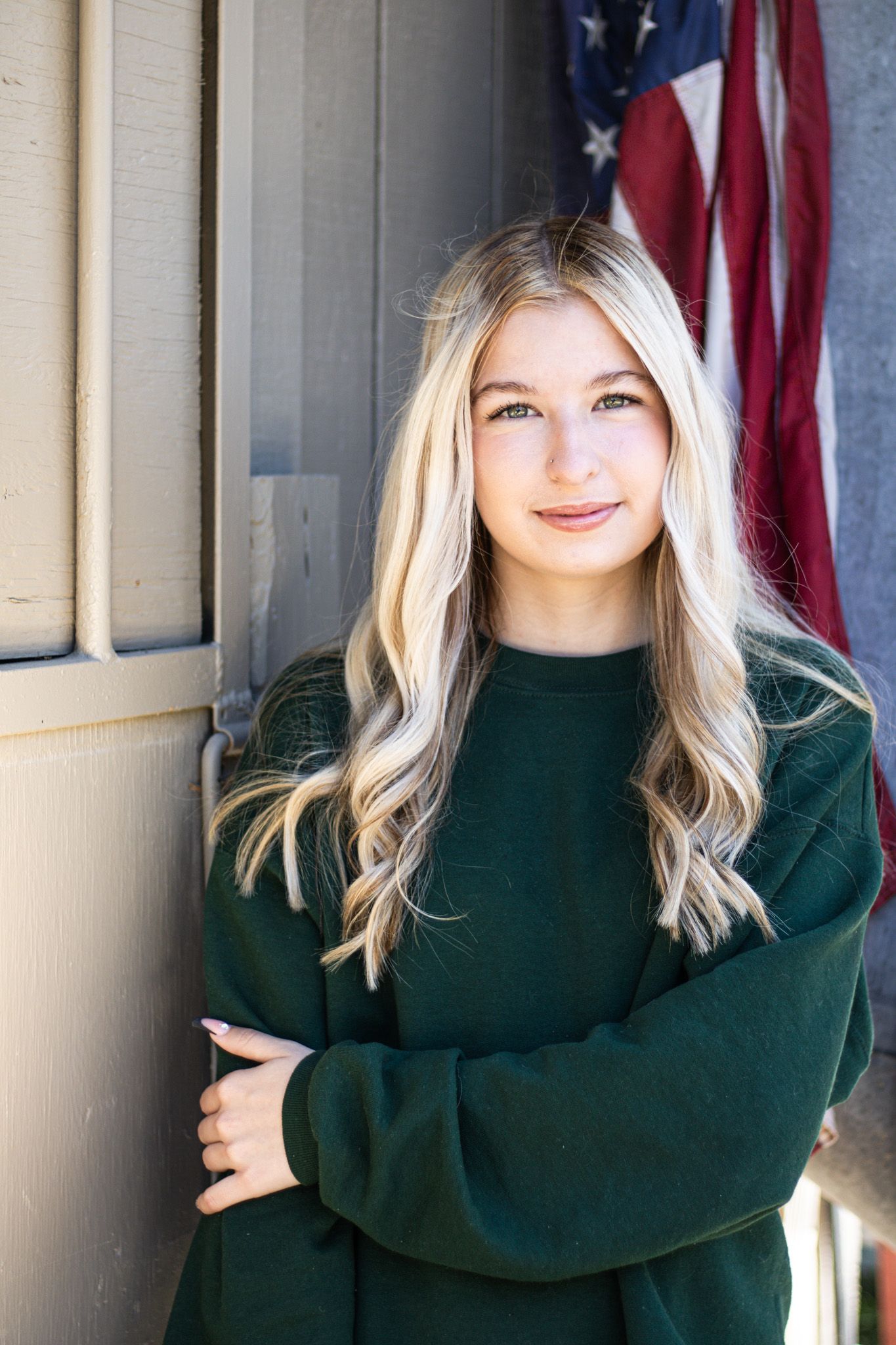 A person in a dark green turtleneck sweater poses against a backdrop with American flags and columns.