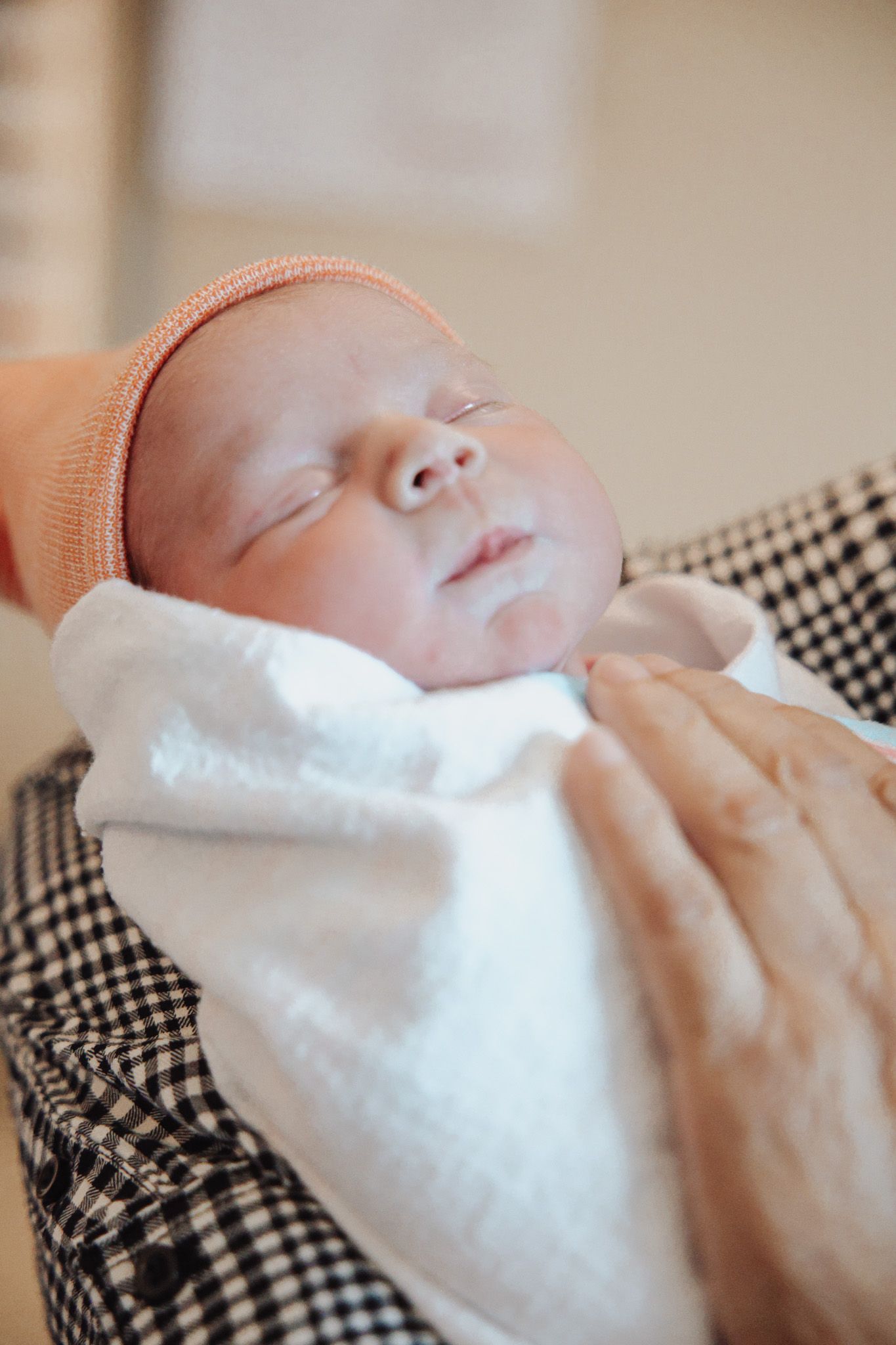 A sleeping newborn baby swaddled in white fabric rests peacefully on a black and white checkered surface.