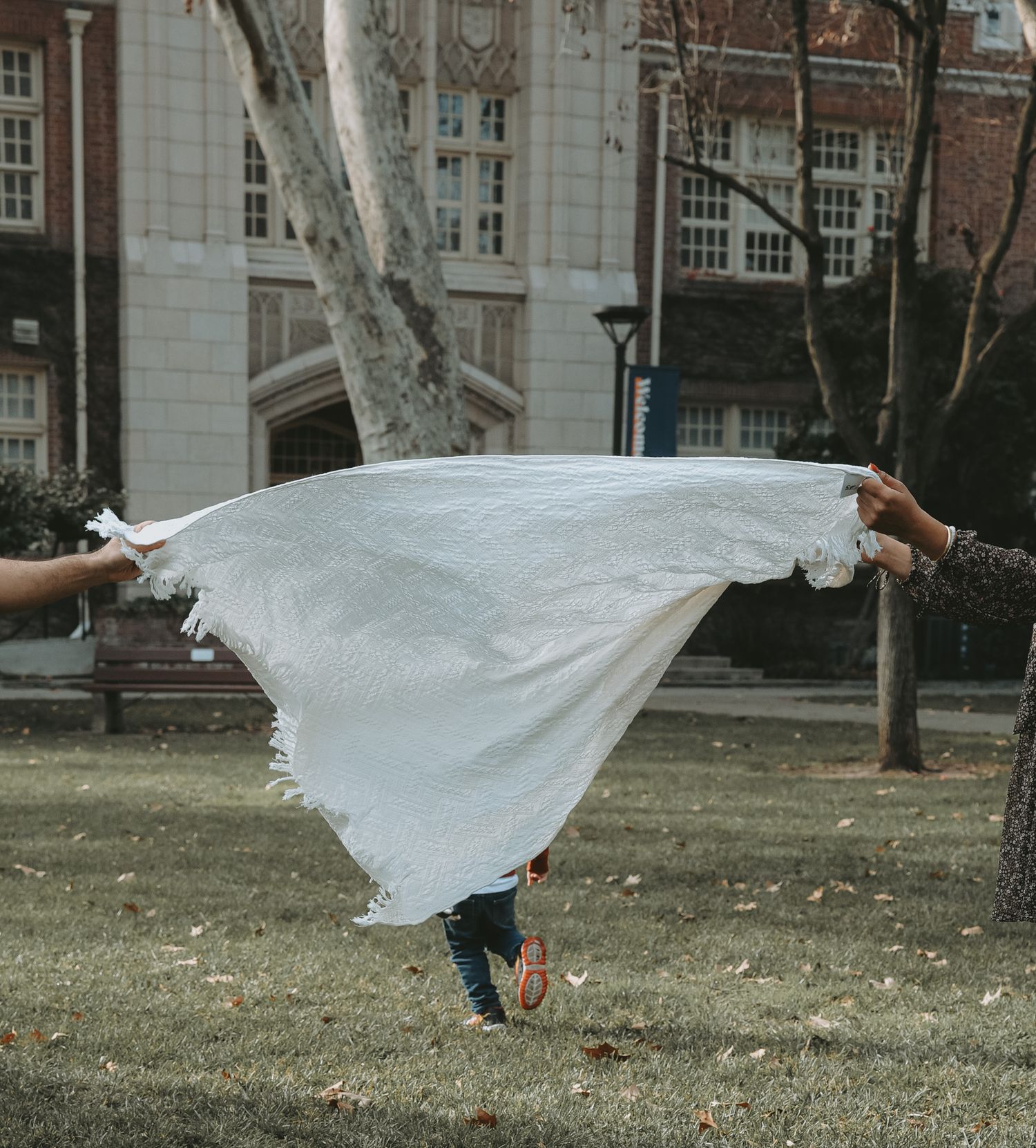 A figure in a flowing white dress performs a graceful dance sequence outdoors on a lawn near buildings.