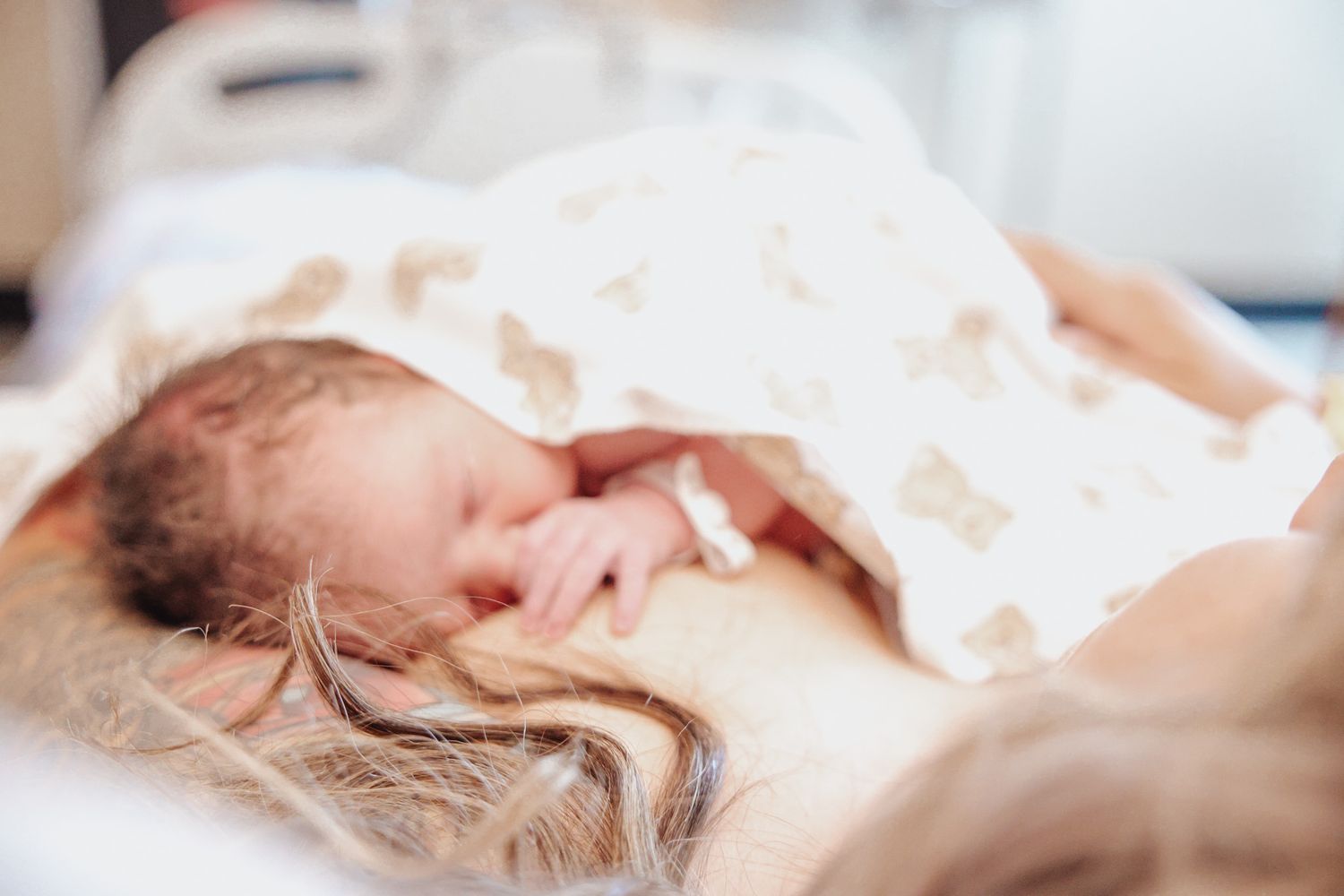 A newborn baby sleeps peacefully under a soft white blanket in a hospital bed.