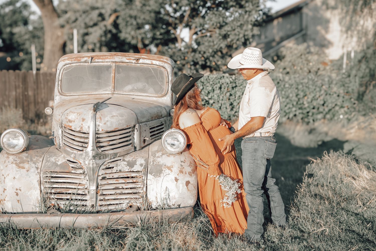 Old rusted vintage cars and automobile parts scattered in grassy outdoor junkyard setting.