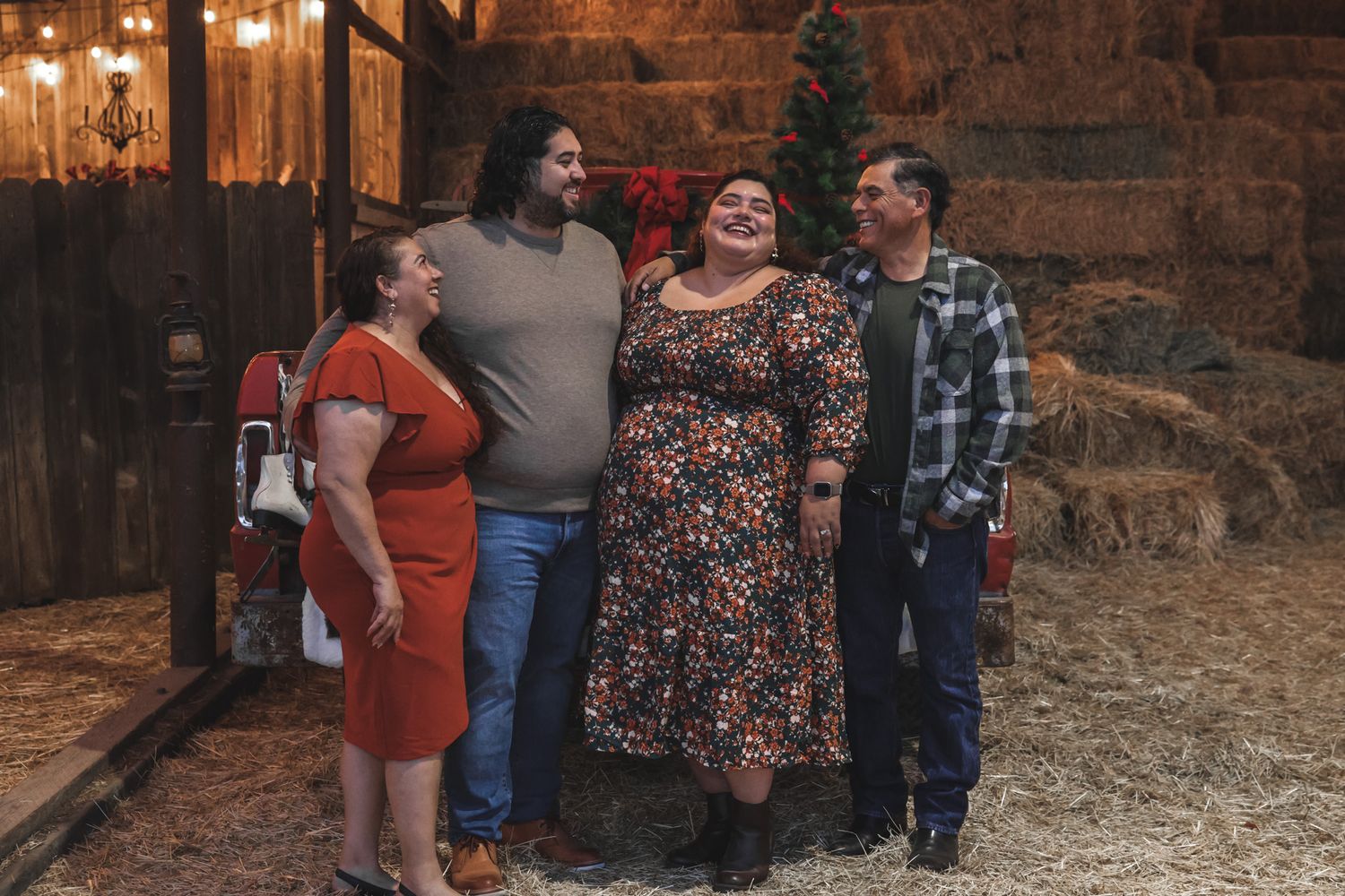 Group of people gathered in a rustic barn setting with warm lighting and hay bales visible in the background.
