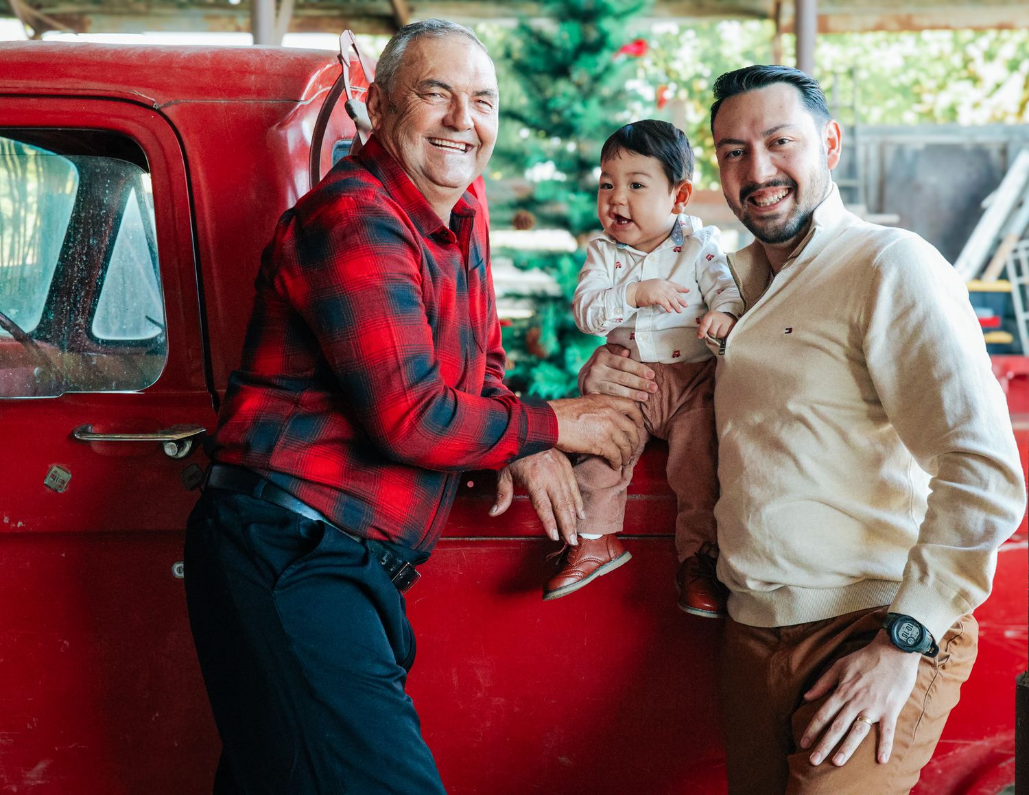 Couple in red plaid and cream outfits share joyful moments together by a vintage red truck during a photo session.