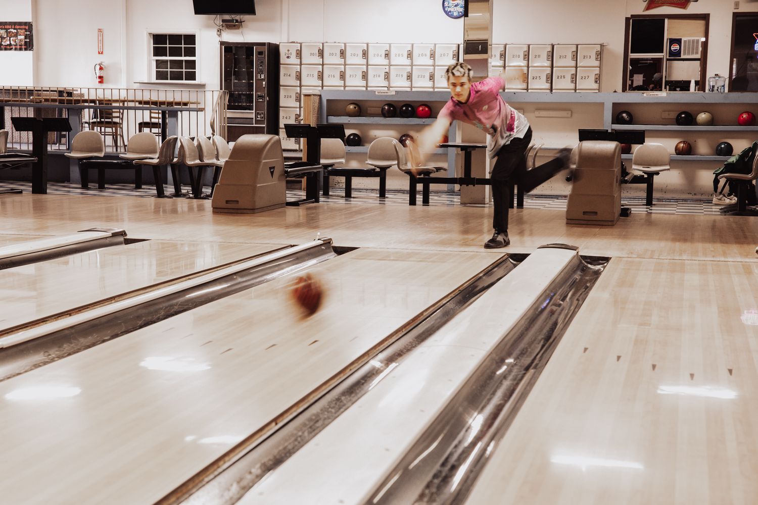 A bowling alley lane with pins set up and a bowling ball rolling down the polished wooden surface.