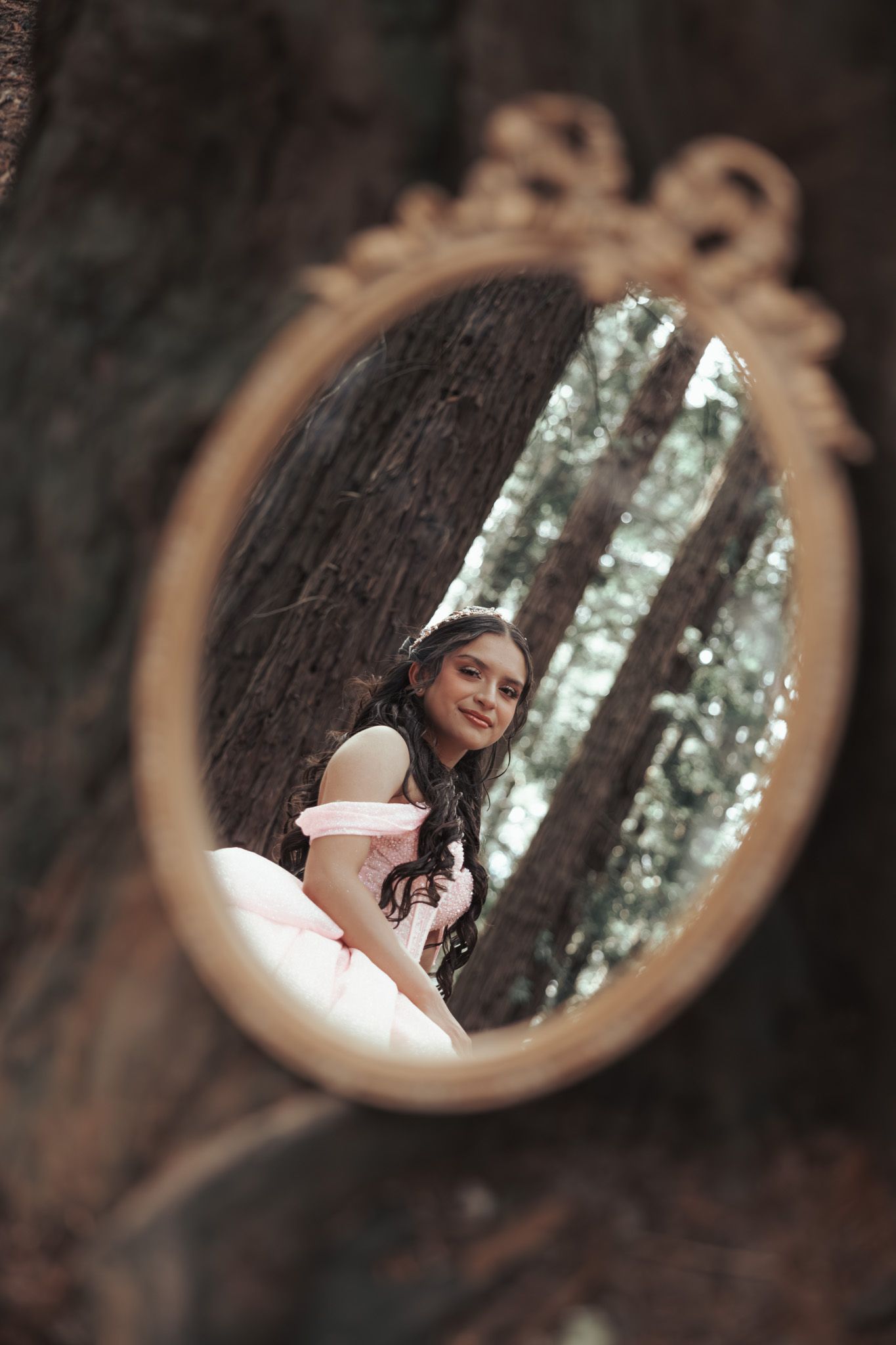 Pre‑quince portrait using a mirror to reflect her face and the tall Oakland redwoods behind her, creating a dreamy forest moment.