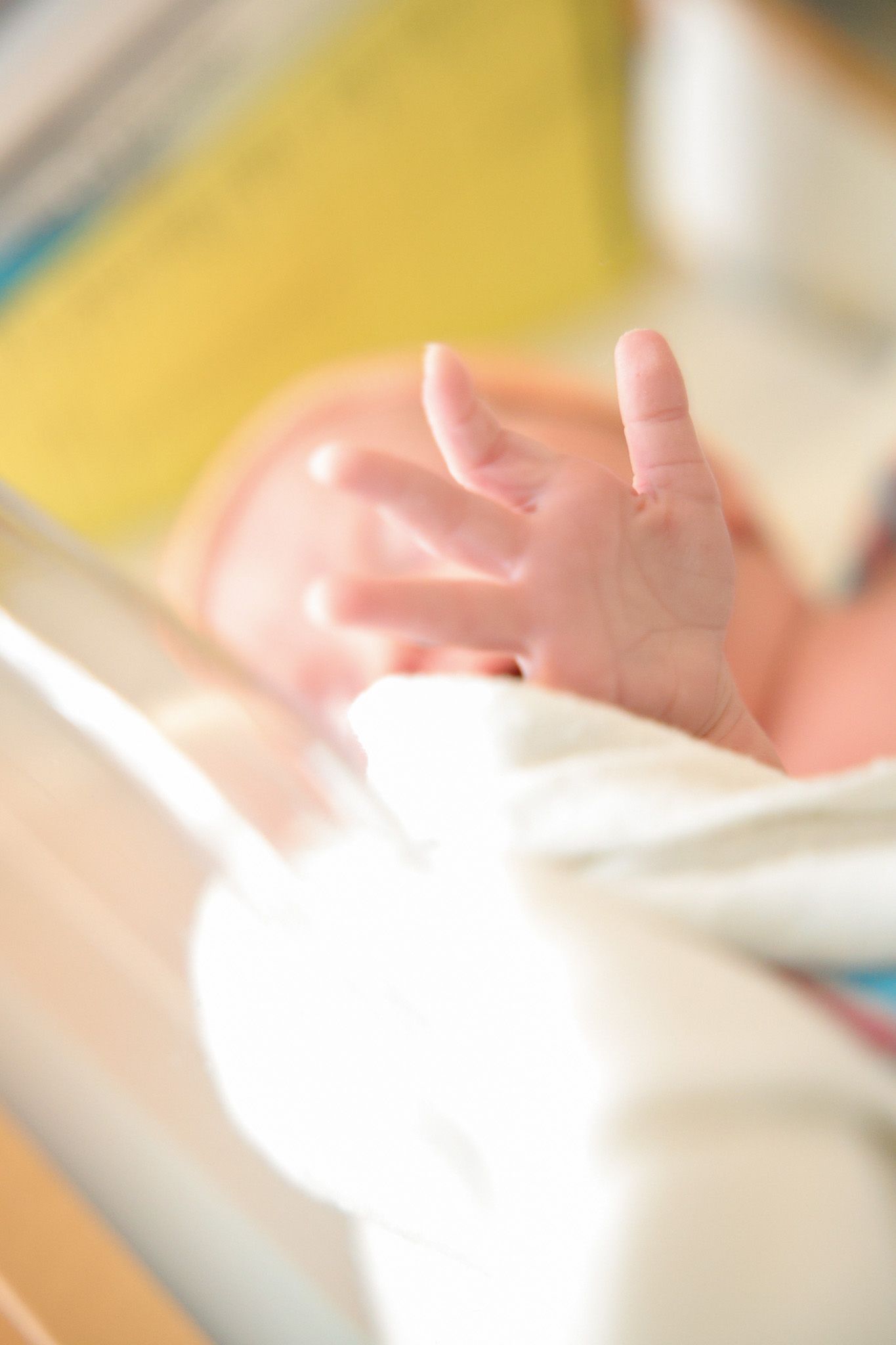 Close-up view of a tiny baby's hand reaching up while wrapped in white blankets.