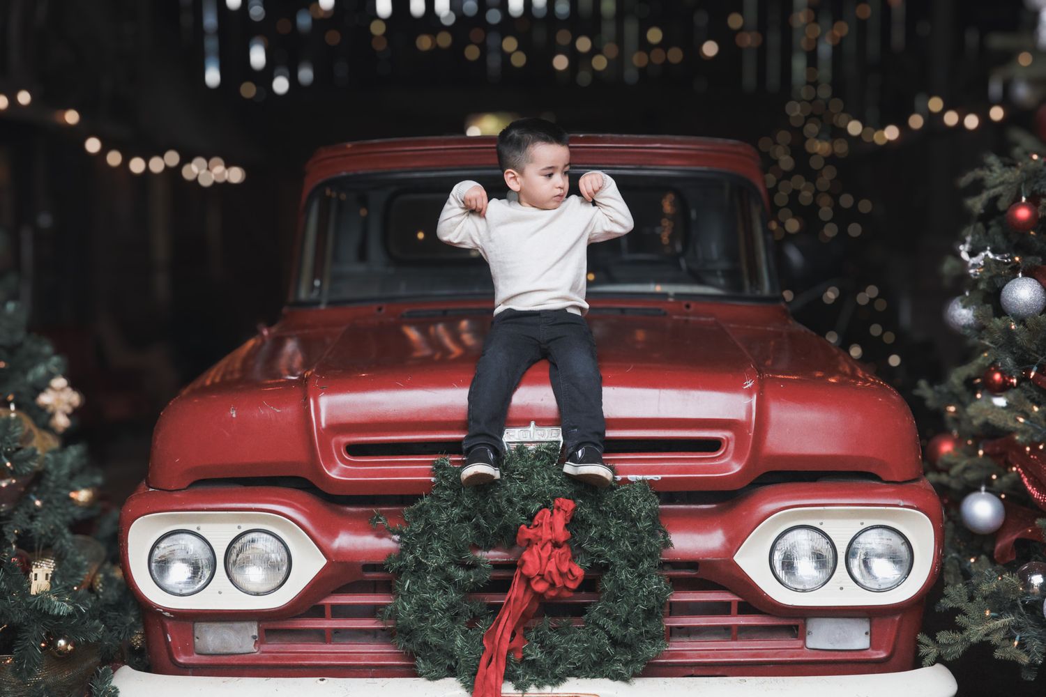 Red classic car decorated with Christmas wreaths and lights creates festive holiday display at night.
