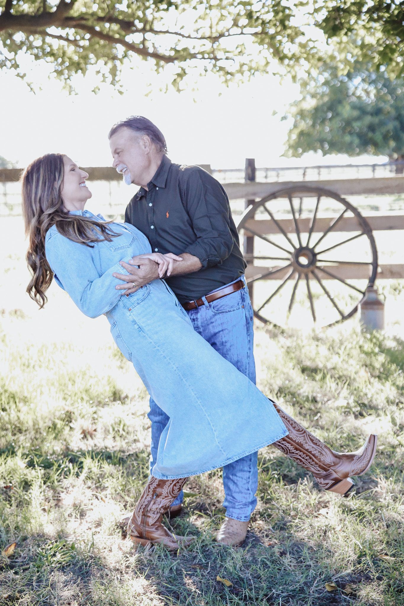 A couple dances playfully in a rustic outdoor setting with a wagon wheel visible in the background.