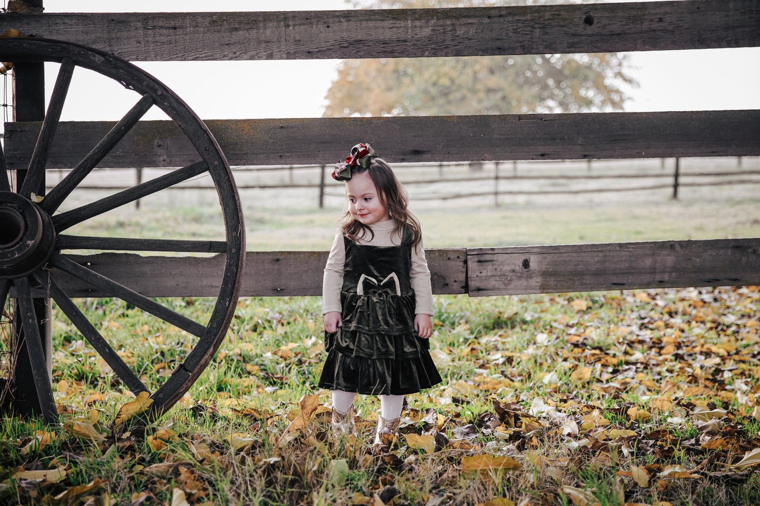 A black dress stands out against a rustic wooden fence backdrop with autumn leaves scattered on the ground.