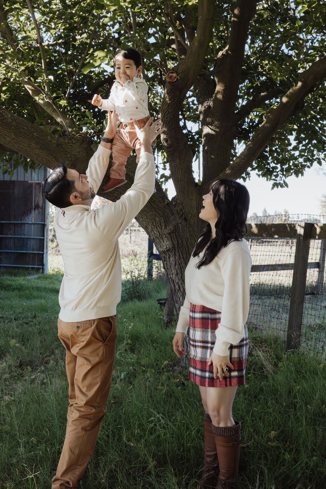 A couple enjoys a playful moment together under a large tree in a grassy outdoor setting.