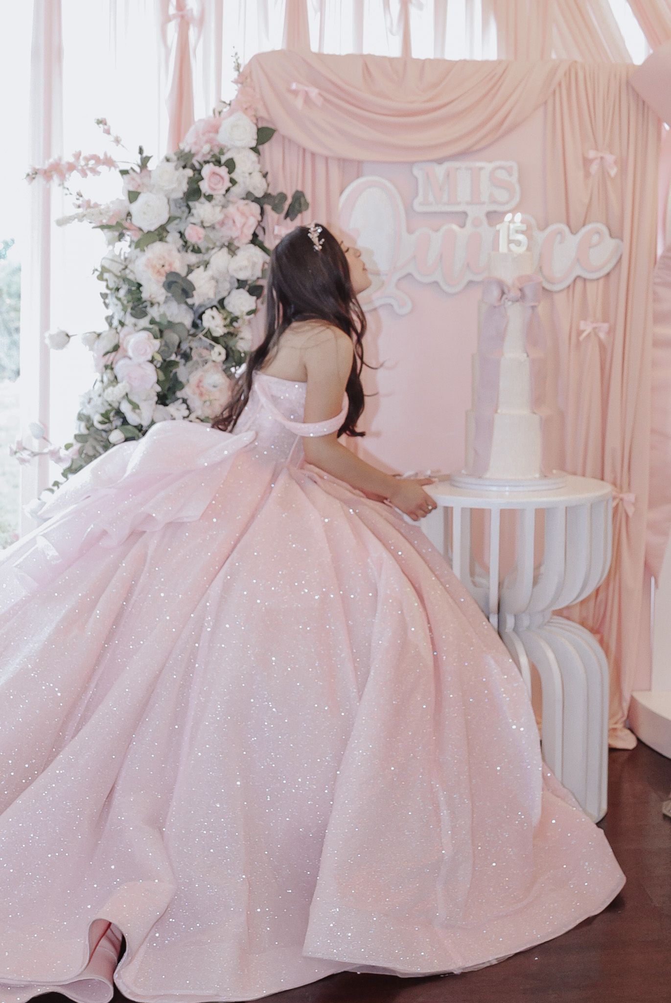 Candid quinceañera photo of the birthday girl leaning over her birthday cake, eyes closed, making a heartfelt wish during the celebration.
