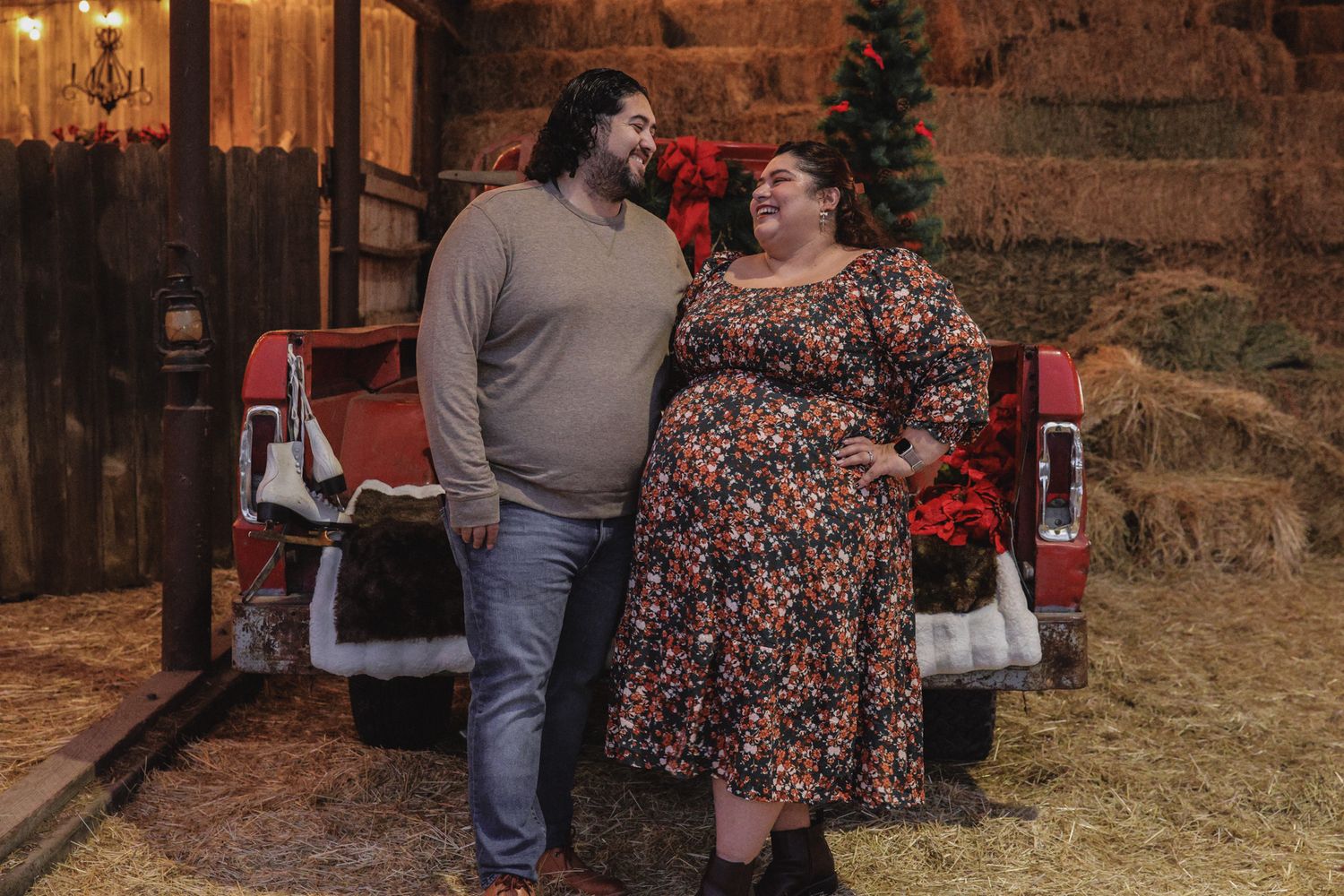 Two people in casual attire stand together in front of a rustic barn setting at sunset.