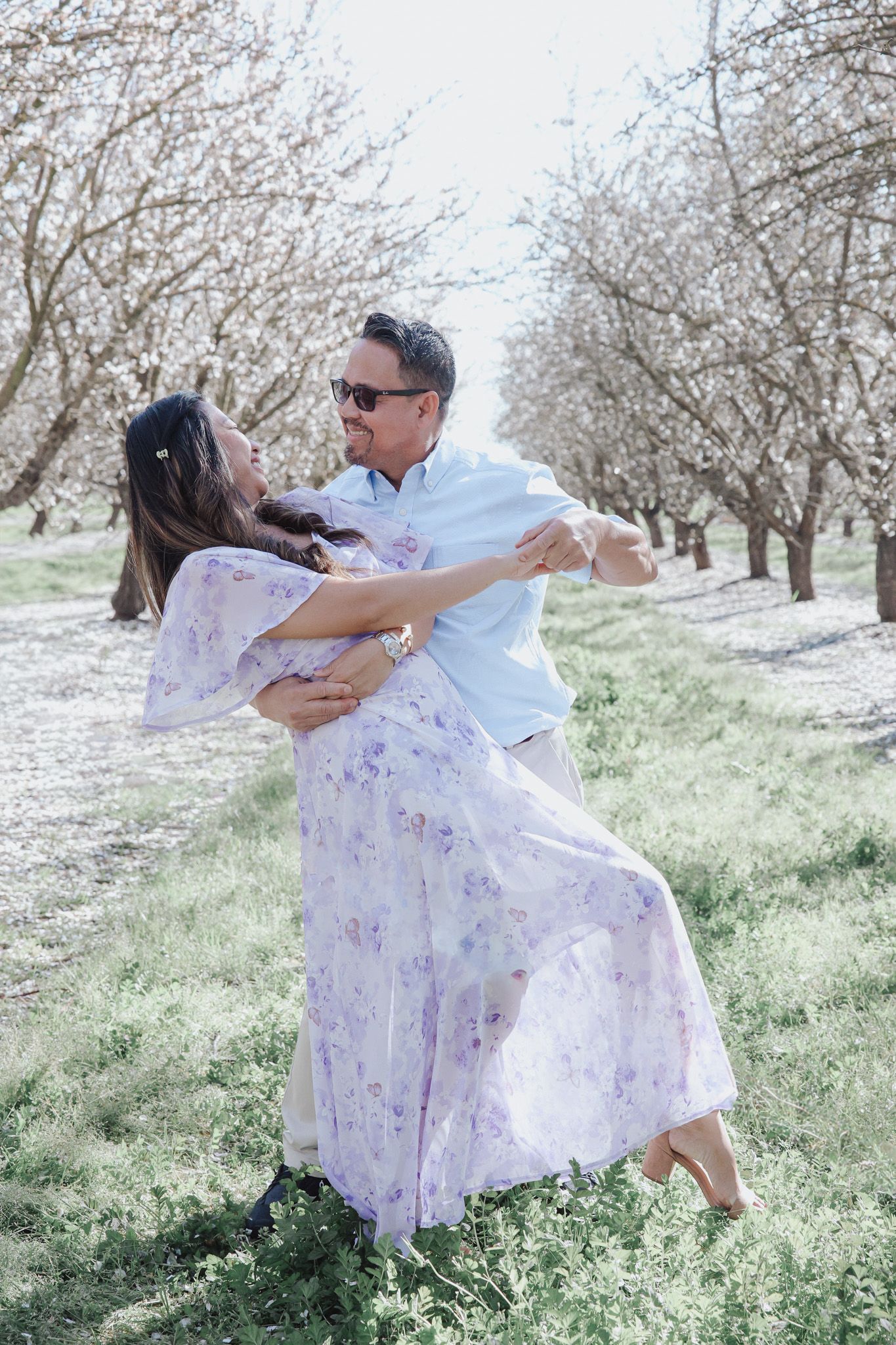 A romantic couple dances together in a blooming almond orchard on a bright spring day.